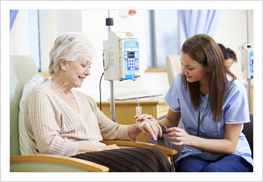 Female Nurse is kneeling down next to an elderly patient who has an iv in her arm